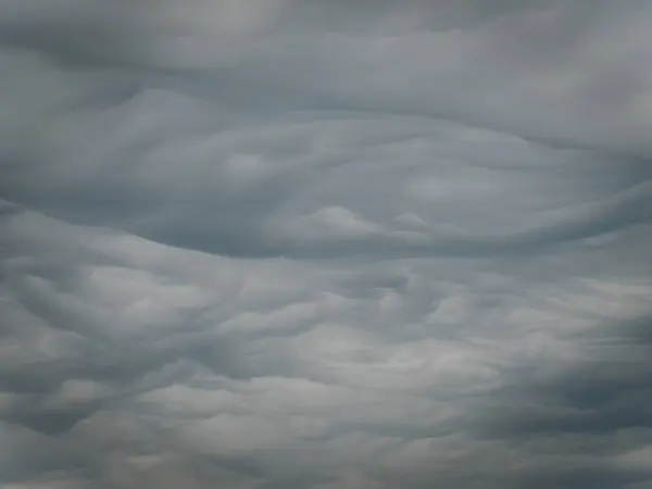 Yoğun, girdap halinde gri renkli fırtına bulutları gökyüzünde dramatik dalga benzeri desenler oluşturur ve yoğun bir atmosfer yaratır. Kopyalama alanı içerir.