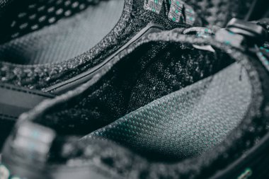 Siyah bir örgü ayakkabının makro görüntüsü, desenli tabanı ve solunabilir dış maddeyi vurguluyor. Konfora ve inşaata detaylı bir göz atmayı teklif ediyor..