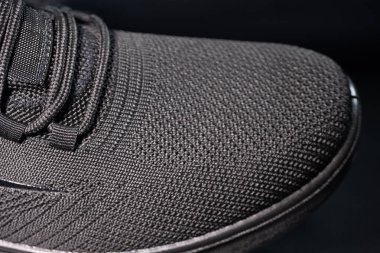 Siyah bir spor ayakkabısının ayrıntılı bir makrosu desenli örgü ayak parmağı, minimalist bağlama sistemi ve şık tasarımı gösteriyor. Modern spor kıyafetleri için mükemmel..