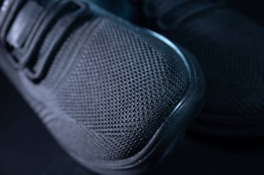 Siyah bir spor ayakkabısının ayrıntılı bir makrosu desenli örgü ayak parmağı, minimalist bağlama sistemi ve şık tasarımı gösteriyor. Modern spor kıyafetleri için mükemmel..