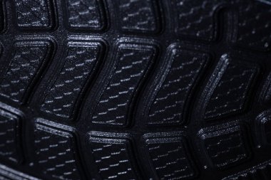 Kavisli oyukları ve geometrik lastik desenli koyu kauçuk bir ayakkabı tabanı, tutuşunu ve dokusunu gösteriyor..