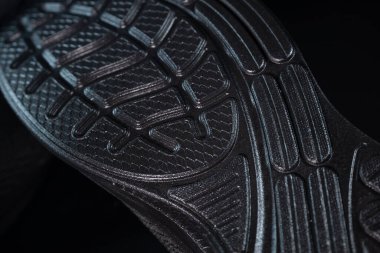 Kavisli oyukları ve geometrik lastik desenli koyu kauçuk bir ayakkabı tabanı, tutuşunu ve dokusunu gösteriyor..