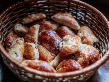 Reçel veya süzme peynir ve etle doldurulmuş çeşitli altın kahverengi hamur işleriyle dolu bir hasır sepetin yakın çekim görüntüsü. Ilık ışıklandırma ev yapımı rahat bir his yaratır..