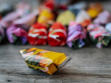 Yakın plan sarı, lale desenli, keskin odak ile sarılı şeker, aşınmış ahşap bir yüzey üzerine yerleştirilmiş, arka planda bulanık, renkli bir şeker çeşitliliği.