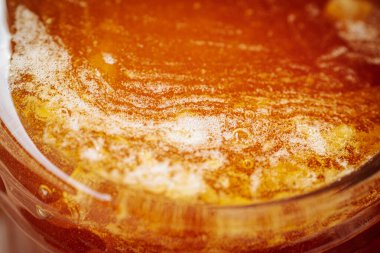 Kırsal bir ahşap yüzeyde cam bir kavanozdaki bala yakın çekim. Balın kendine özgü dokusu ve kehribar rengi.