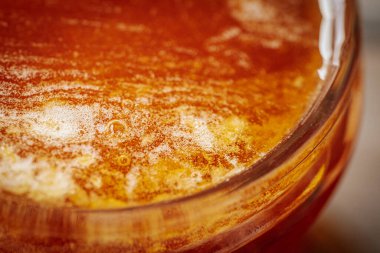 Kırsal bir ahşap yüzeyde cam bir kavanozdaki bala yakın çekim. Balın kendine özgü dokusu ve kehribar rengi.