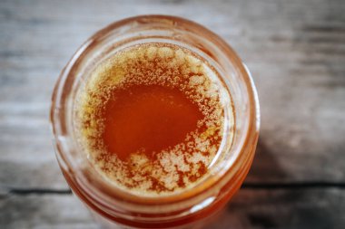 Kırsal bir ahşap yüzeyde cam bir kavanozdaki bala yakın çekim. Balın kendine özgü dokusu ve kehribar rengi.