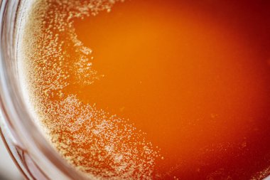 Kırsal bir ahşap yüzeyde cam bir kavanozdaki bala yakın çekim. Balın kendine özgü dokusu ve kehribar rengi.