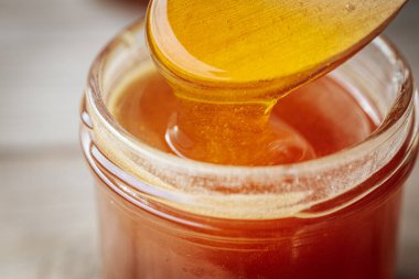 Bir kaşıktan cam bir kavanoza damlayan altın bal, zengin, pürüzsüz dokusunu ve doğal rengini gözler önüne seriyor. Sıcak tonlar kompozisyona hakim..