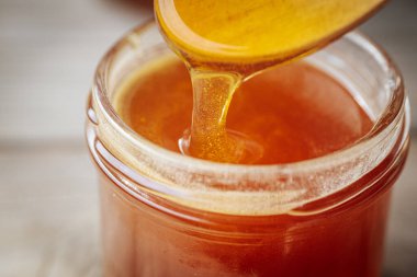 Bir kaşıktan cam bir kavanoza damlayan altın bal, zengin, pürüzsüz dokusunu ve doğal rengini gözler önüne seriyor. Sıcak tonlar kompozisyona hakim..