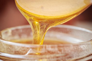 Bir kaşıktan cam bir kavanoza damlayan altın bal, zengin, pürüzsüz dokusunu ve doğal rengini gözler önüne seriyor. Sıcak tonlar kompozisyona hakim..