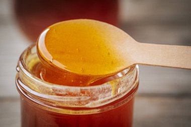 Bir kaşıktan cam bir kavanoza damlayan altın bal, zengin, pürüzsüz dokusunu ve doğal rengini gözler önüne seriyor. Sıcak tonlar kompozisyona hakim..