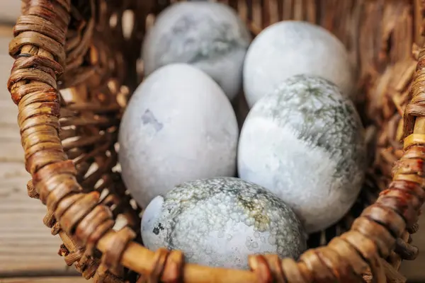 Gri, yeşil ve beyaz tonlarında mermer desenli birkaç yumurtayı hasır bir sepete koy. Toprak tonları ve doğal aydınlatma.