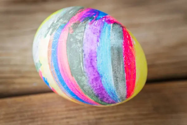 Ahşap bir yüzeye yerleştirilmiş kalın gökkuşağı çizgileriyle süslenmiş renkli bir Paskalya yumurtasının yakın çekimi. Parlak ve şenlikli, el yapımı bir his..