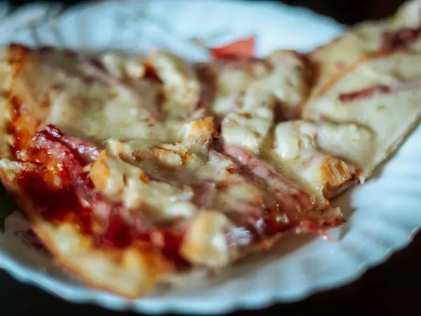 Beyaz bir tabakta servis edilen iki dilim peynirli pizza ve erimiş peynirin yakın çekimi. Sıcak ışıklandırmalı yumuşak odak arkaplanı.