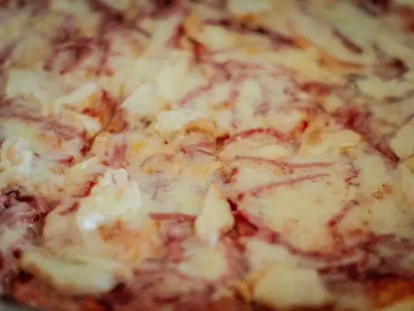 Eritilmiş peynir ve jambon şeritli dilimlenmemiş bir pizzanın yakın çekimi. Yüzey altın ve hafif çıtır, doku ve renge odaklı..