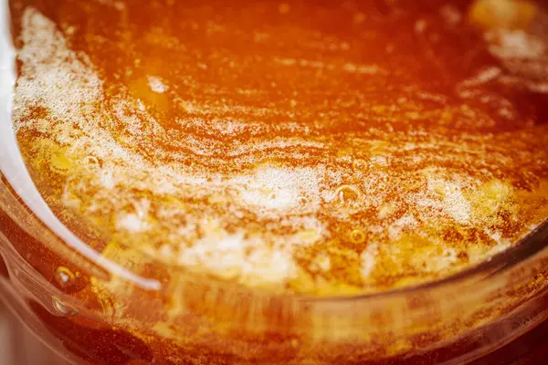 Kırsal bir ahşap yüzeyde cam bir kavanozdaki bala yakın çekim. Balın kendine özgü dokusu ve kehribar rengi.