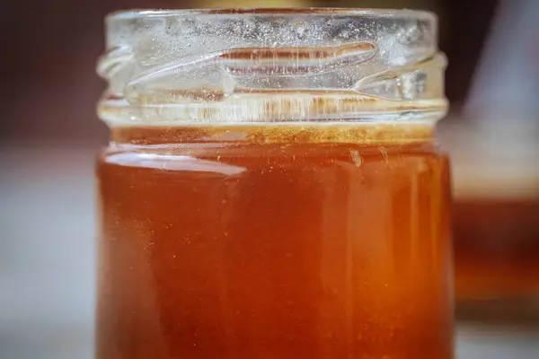 Altın kehribar balı ile dolu cam kavanozların yakın plan çekimleri. Kırsal ahşap bir yüzeye yerleştirilmiş ve arka planda bulanıklık var..