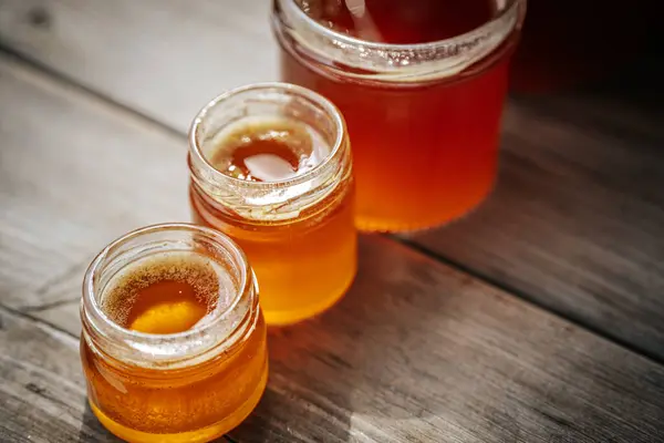 Altın kehribar balı ile dolu cam kavanozların yakın plan çekimleri. Kırsal ahşap bir yüzeye yerleştirilmiş ve arka planda bulanıklık var..