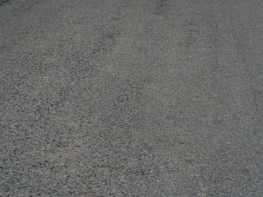 Görünür kümeler ve küçük çakıl taşlarıyla desenli asfalt yol yüzeyinin detaylı görüntüsü. Doğal ışıklandırma.
