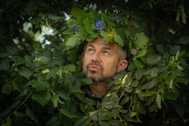 Meşe yaprakları ve kır çiçeklerinden oluşan bir çelenk içindeki oyuncu bir adam yoğun yaprakların arasından çıkar ve mizahı doğayla birleştirerek öpücüklü bir yüz yapar..