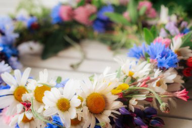 Yumuşak odaklı çiçek arkaplanlı hafif ahşap bir yüzeye yerleştirilmiş papatya, çiçek ve yonca renginde bir çelengin ayrıntılı bir yakın çekimi..