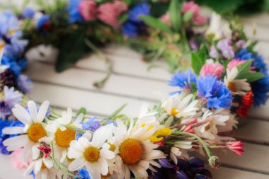 Yumuşak odaklı çiçek arkaplanlı hafif ahşap bir yüzeye yerleştirilmiş papatya, çiçek ve yonca renginde bir çelengin ayrıntılı bir yakın çekimi..