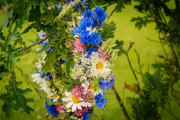 Yaban çiçekleri ve meşe yapraklarından yapılmış el yapımı bir çelenk açık havada yeşil bir ortamda asılı duruyor..