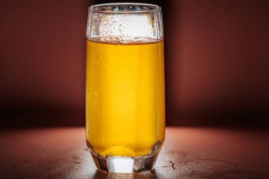 Canlı, karbonatlı turuncu bir içecekle dolu berrak bir bardak görünür kabarcıklar ve koyu bir arka planda parlayan bir görünüm..