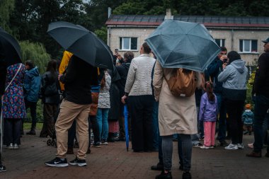 Bir grup insan yağmurlu bir havada açık havada şemsiye ve yağmurluğun altında birbirlerine yakın dururlar..