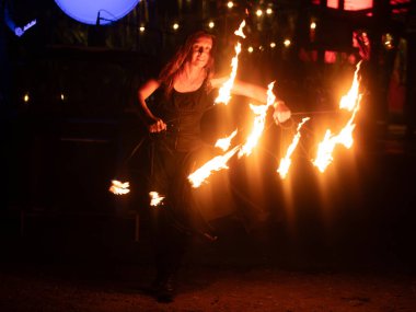 Kırmızı-turuncu alevler ve arka planda canlı bir grupla dramatik bir gece performansında iki ateş dansçısı alevli aksesuar çevirir..