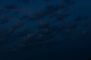 Büyük, karanlık bir bulut, soluk pembe ışıkla renklendirilmiş, derin bir alacakaranlık gökyüzünde süzülür. Metin için geniş bir alanı olan minimalist, karamsar bir sahne yaratır..