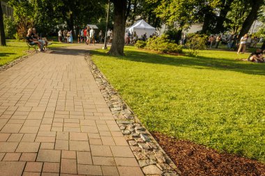 Kalabalık bir grup, açık hava parkında yemek stantları, afişler ve şenlikli bir yaz akşamı atmosferiyle dolaşır ve kaynaşır.. 
