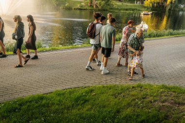 İnsanlar, sakin ve manzaralı bir yaz anının tadını çıkararak, altın akşam ışığında, ağaçların oluşturduğu göl yolu boyunca kürek çekerek gezerler. Valmiera, Letonya - 02.08.2025
