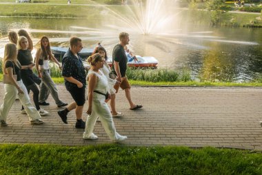 İnsanlar, sakin ve manzaralı bir yaz anının tadını çıkararak, altın akşam ışığında, ağaçların oluşturduğu göl yolu boyunca kürek çekerek gezerler. Valmiera, Letonya - 02.08.2025