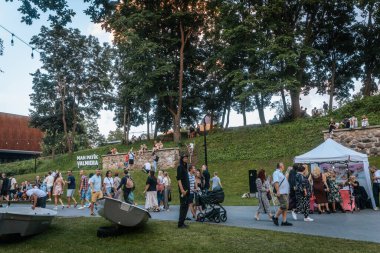 Bir grup insan, Letonya, Valmiera 'daki nehir kıyısında, suda kayıklar ve büyük 