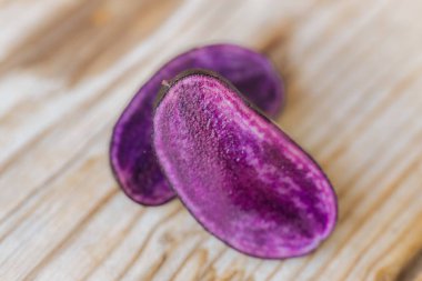 Mor bir patates diliminin makro çekimi yüzeyindeki parlak dokuyu ve nemi ahşap bir zemine karşı gösteriyor. Doğal ışıklandırma ve sığ alan derinliği.