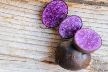 Açık renkli, ahşap bir yüzeye yerleştirilmiş, geniş bir kopya alanı ve doğal ışıklandırması olan mor bir patates..