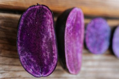 Kırsal ahşap tahtalarda sergilenen mor patateslerin parlak kesitleri, onların derin renklerini ve doğal mermer şekillerini vurguluyor..