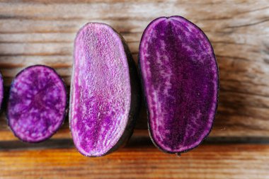 Kırsal ahşap tahtalarda sergilenen mor patateslerin parlak kesitleri, onların derin renklerini ve doğal mermer şekillerini vurguluyor..