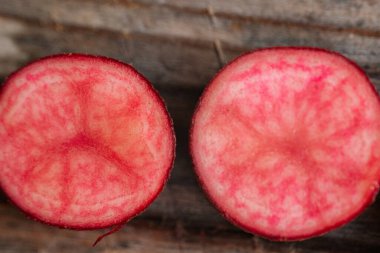 Kırsal ahşap bir zemine yerleştirilmiş, parlak pembe ve kırmızı bilyeli iki kırmızı patatesin kesiti..