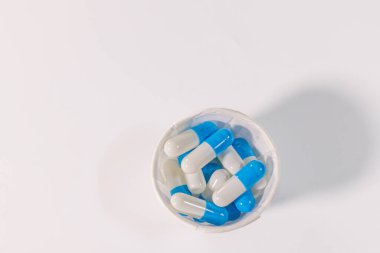 Beyaz bir yüzeye yerleştirilmiş mavi ve beyaz kapsüllerle dolu küçük bir kağıt bardak ve metin için bolca yer var. Tıbbi ya da ilaç teması.