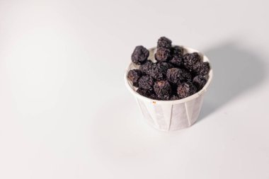 Beyaz bir yüzeye yerleştirilmiş kurumuş böğürtlenlerle dolu beyaz bir kağıt bardak..