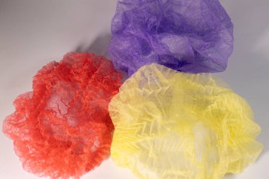 Kırmızı, sarı ve mor renkli üç tek kullanımlık saç filesi, açık bir yüzeye yayılmış, şeffaf ve dokulu yapılarını ortaya koyuyor..