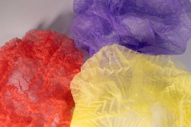 Kırmızı, sarı ve mor renkli üç tek kullanımlık saç filesi, açık bir yüzeye yayılmış, şeffaf ve dokulu yapılarını ortaya koyuyor..