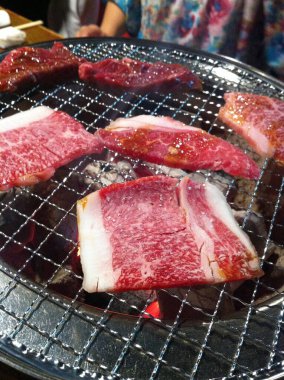 Bir Yakiniku restoranında geleneksel kömür ızgarasına çiğ et dilimleri yerleştirilir..