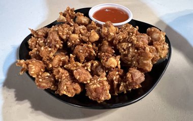 Acı sosla servis edilen çıtır susamlı tavuk tendonları.