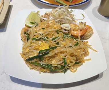 Taze sebze ve limonla servis edilen karides ve kalamarlı Pad Thai.