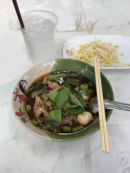 Baharatlı domuz suyuyla Tayland pilavı çorbası, sabah zaferi ve fesleğenle kaplanmış, çiğ fasulye filizi ile servis edilmiş..