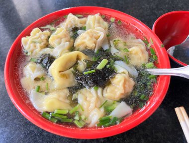 Temiz çorba, karides mantı, yosun ve soğanla dolu kırmızı bir kase.